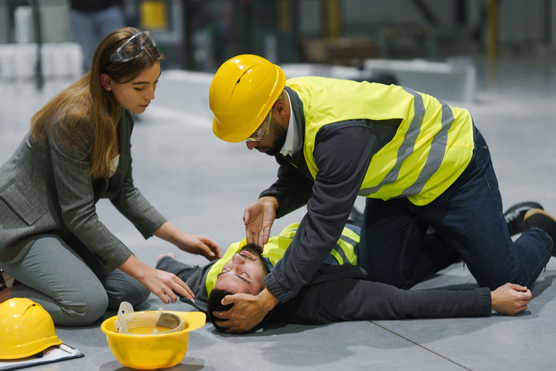 A man and a woman are helping a construction worker who has fallen on the floor. A man and a woman are helping a construction worker who has fallen on the floor.