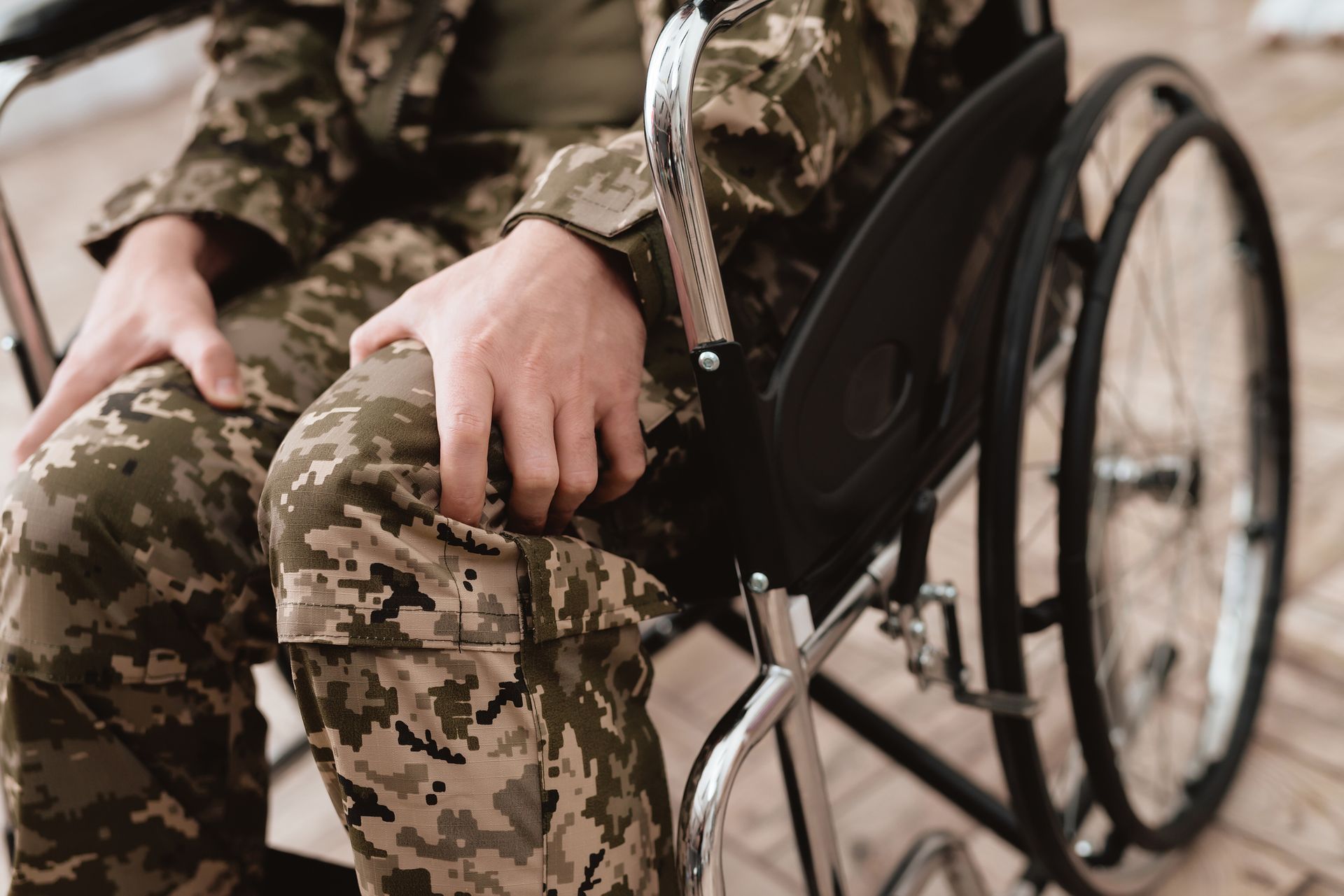 A soldier is sitting in a wheelchair with his hands on his knees.