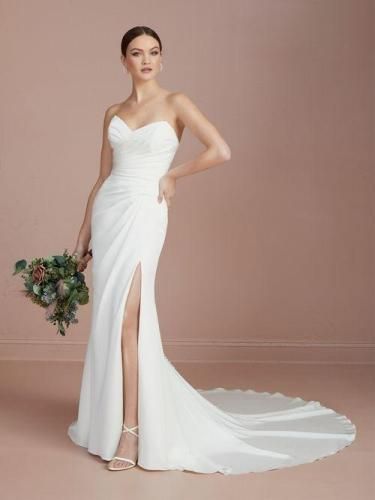 Woman in a white strapless wedding dress with a thigh-high slit, holding flowers.