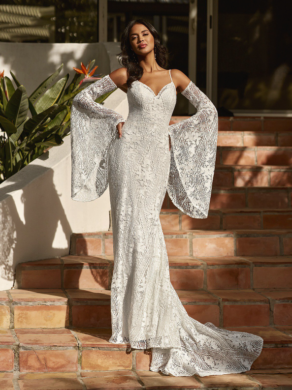 Woman in white lace wedding dress with long sleeves, posing on outdoor steps.