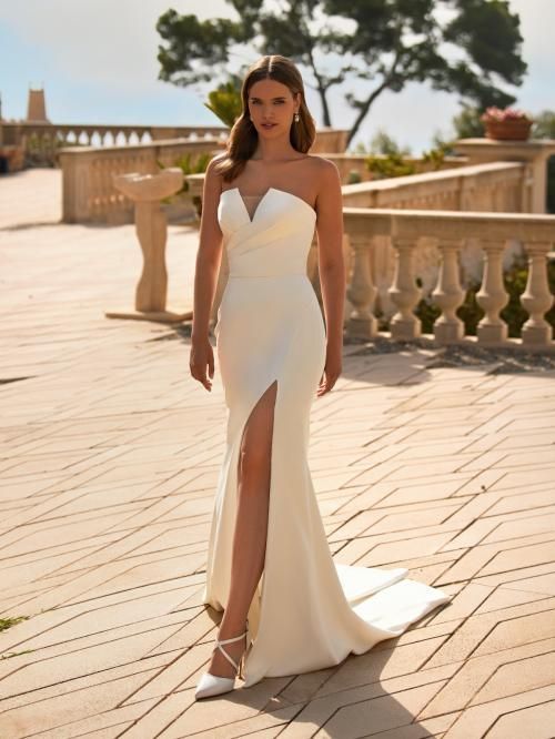 Woman in strapless white wedding dress with slit, standing on patio.