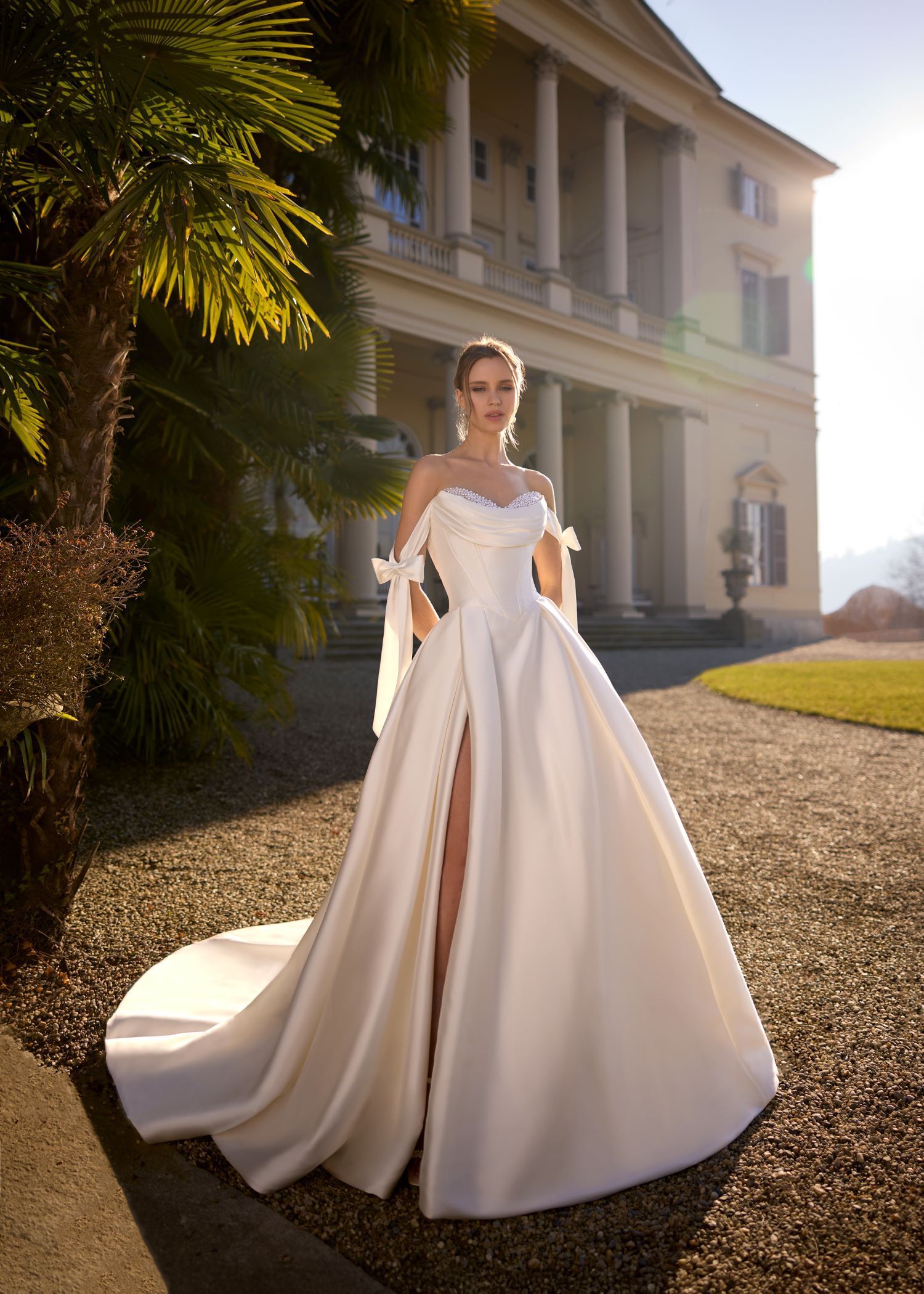 Bride in white gown with high slit posing outdoors in front of a classical building.