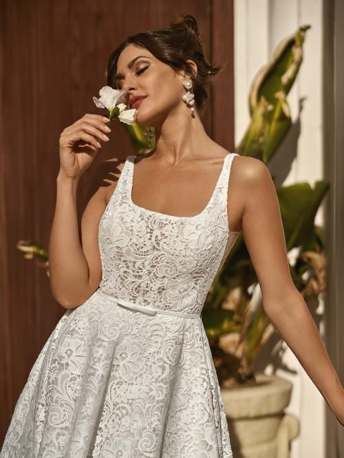 Woman in white lace dress holding a flower, eyes closed, sunlit outdoors.