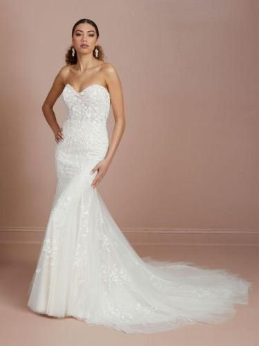 Woman in strapless white wedding dress with lace detail and long train, posing indoors.