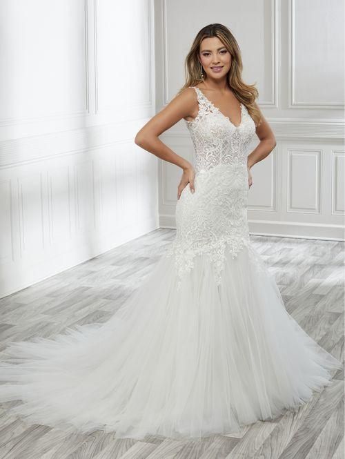 Woman in a white lace and tulle mermaid wedding dress. She is smiling, posing in a room with wood floors.