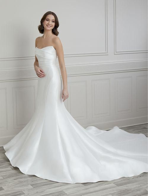 Woman in a white strapless wedding gown with a flowing train, standing in front of a wall with decorative molding.