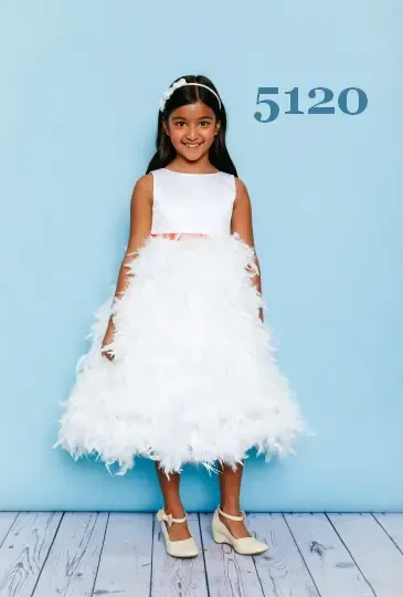 Woman in a dark, sparkling off-shoulder dress, posing by a window with a light, open-air background.