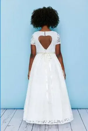 Girl in white dress with heart-shaped back cutout; light blue backdrop, wooden floor.