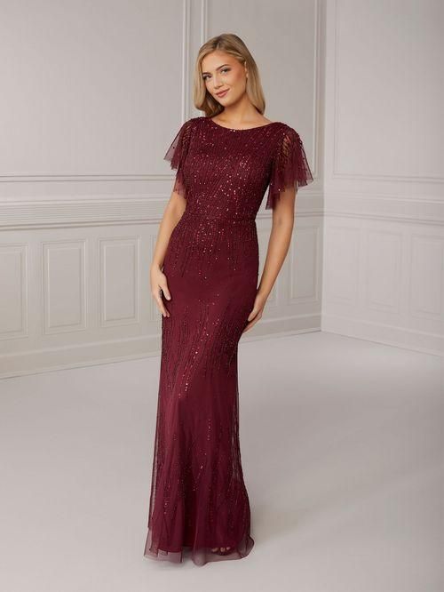 Woman in a maroon sequined gown with flutter sleeves, standing in a bright room.