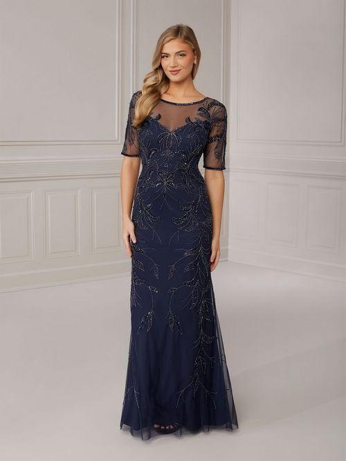 Woman in navy blue beaded gown with sheer neckline and sleeves. Standing in a bright room.