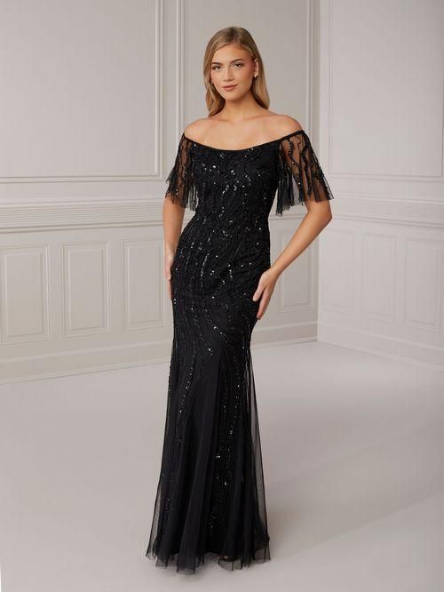 Woman in a black off-the-shoulder gown with beading, standing in a room with light walls.