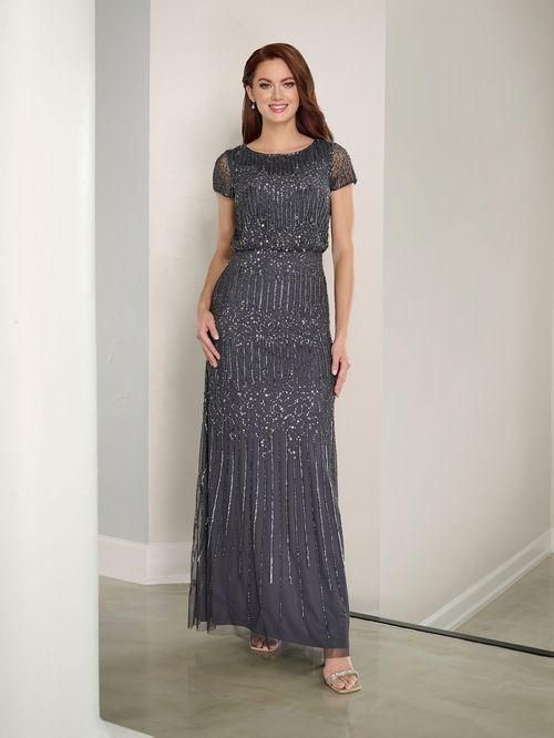 Woman in beaded gray formal gown, standing in neutral setting with a smile.