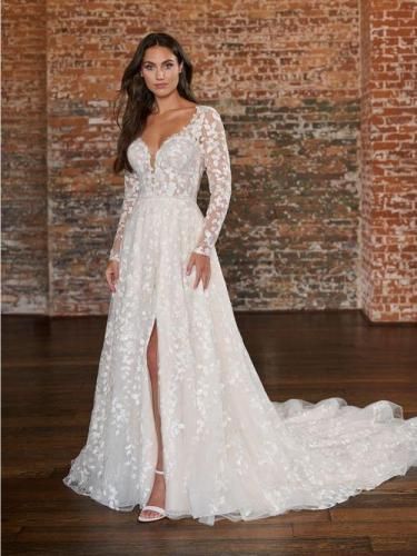 Woman in white wedding dress with long sleeves and slit, posing in front of a brick wall.