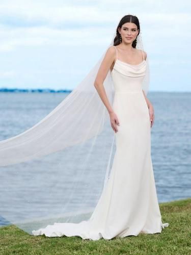 Woman in a white wedding dress with a long veil standing by the ocean.