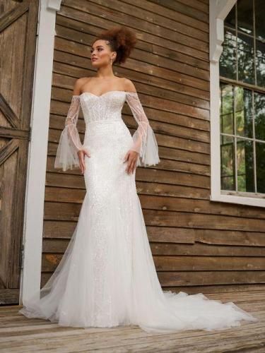 Woman in white off-shoulder wedding dress, with bell sleeves, posing on wooden porch.