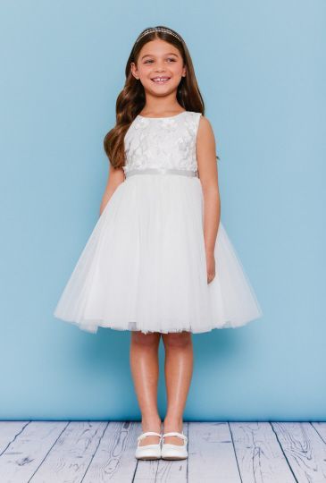 Girl in a white dress, smiling, against a blue backdrop. She's wearing a headband and shoes.