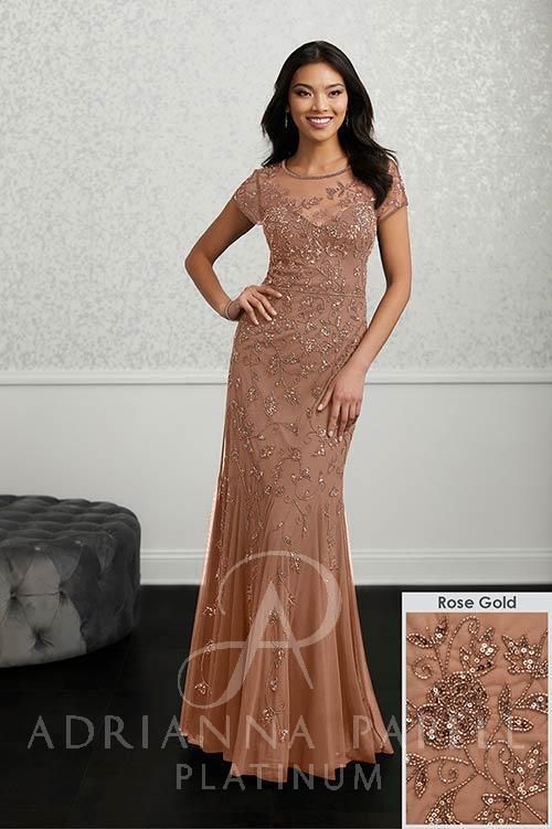 Woman in rose gold beaded formal gown, standing indoors, smiling.