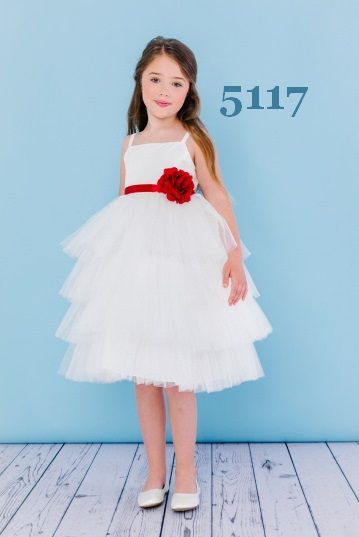 Girl in white tiered dress with red flower belt and white shoes; standing in front of a blue backdrop.