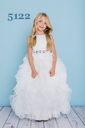Girl in white dress with ruffled skirt, smiling, in front of a light blue backdrop.