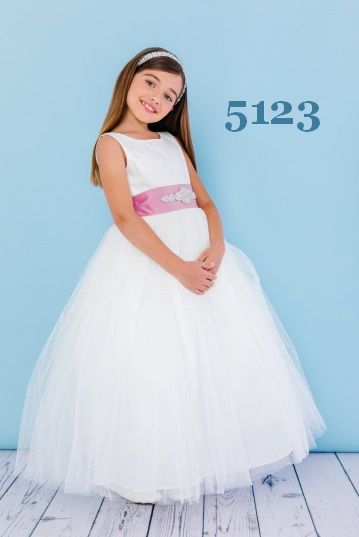 Girl in white dress with pink sash and silver tiara smiles against a blue backdrop, with the number