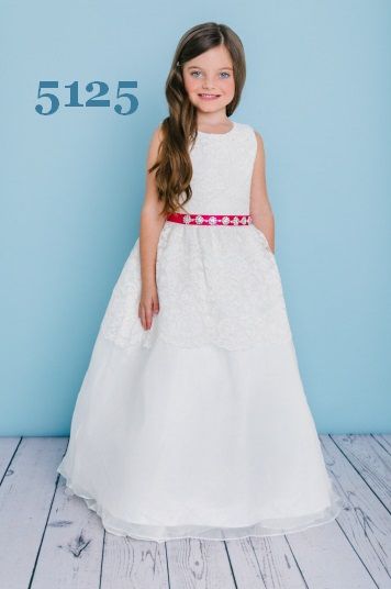 Girl in a white dress with a red belt, smiling, in front of a blue backdrop.