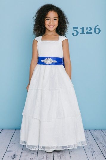 Girl in white dress with blue sash, standing against a blue background.