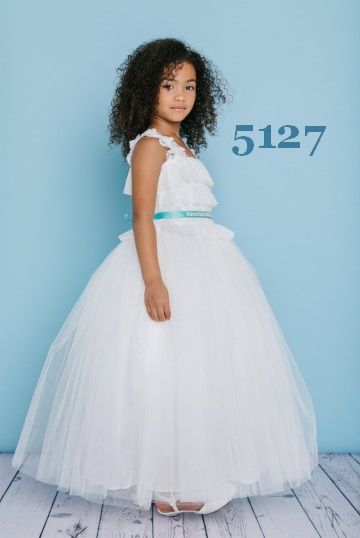 Girl in white formal dress with teal sash, stands in front of light blue background.