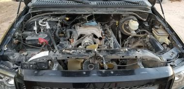 Engine compartment of a black vehicle, hood open. Several components are visible and covered with a white substance.