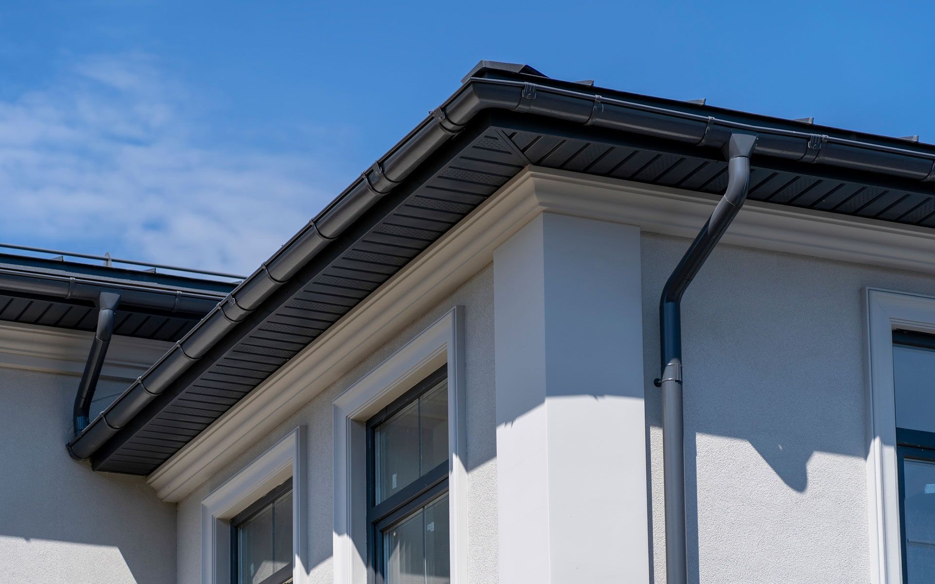 A white house with a black gutter on the roof.