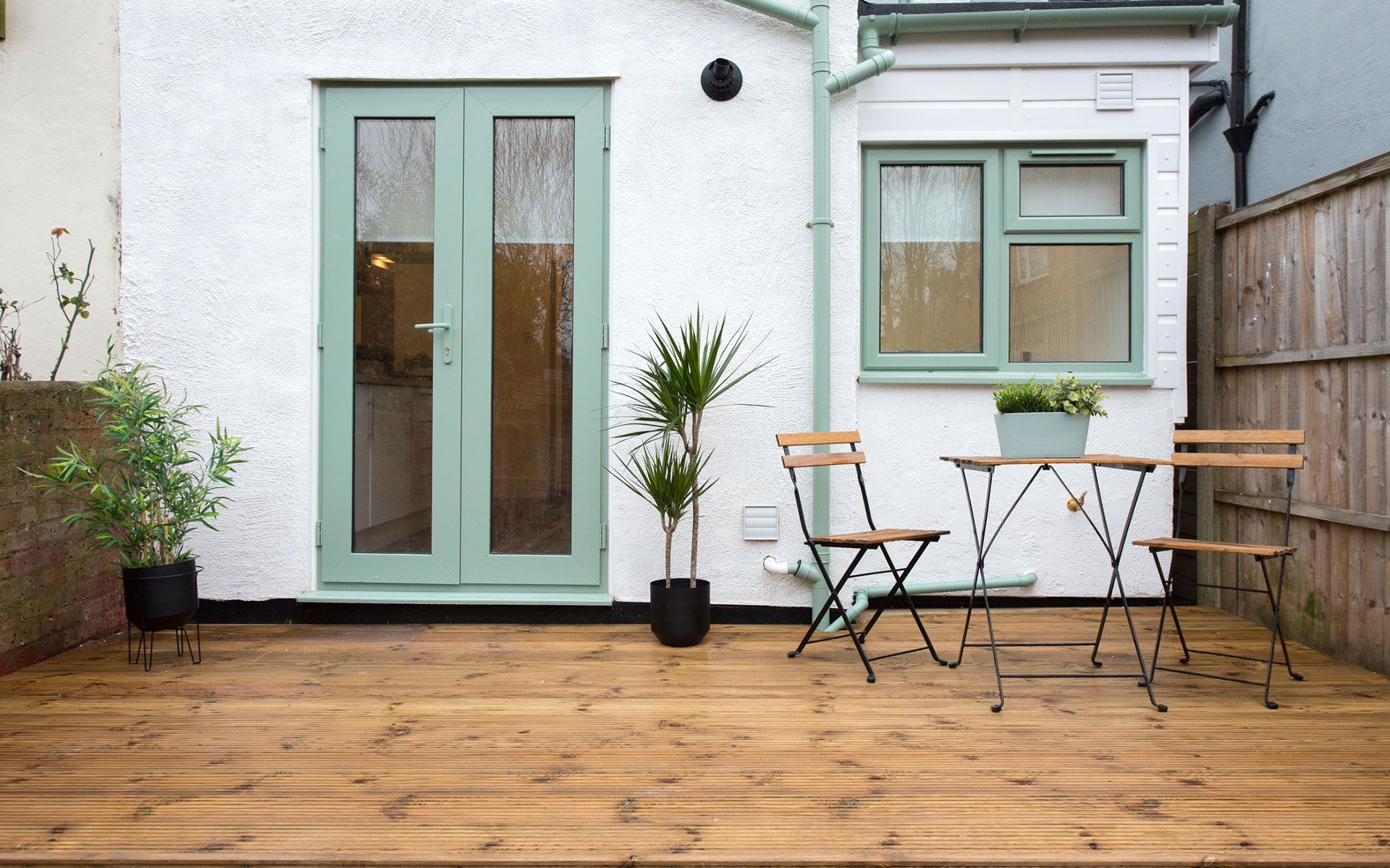 A wooden deck with a table and chairs in front of a white house.