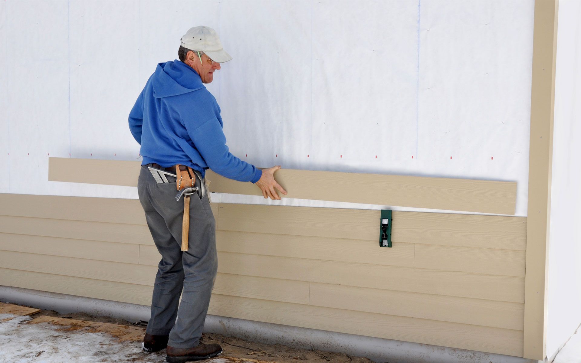 A man is measuring a piece of siding on a wall.