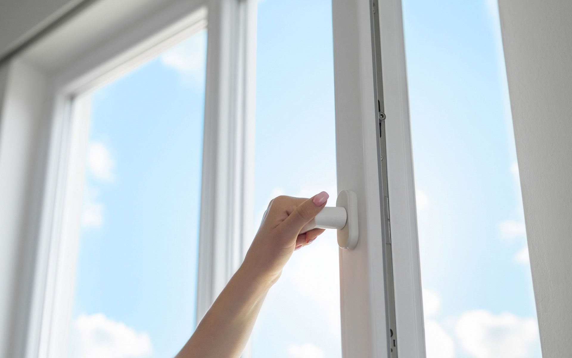 A woman is opening a window with a blue sky in the background.