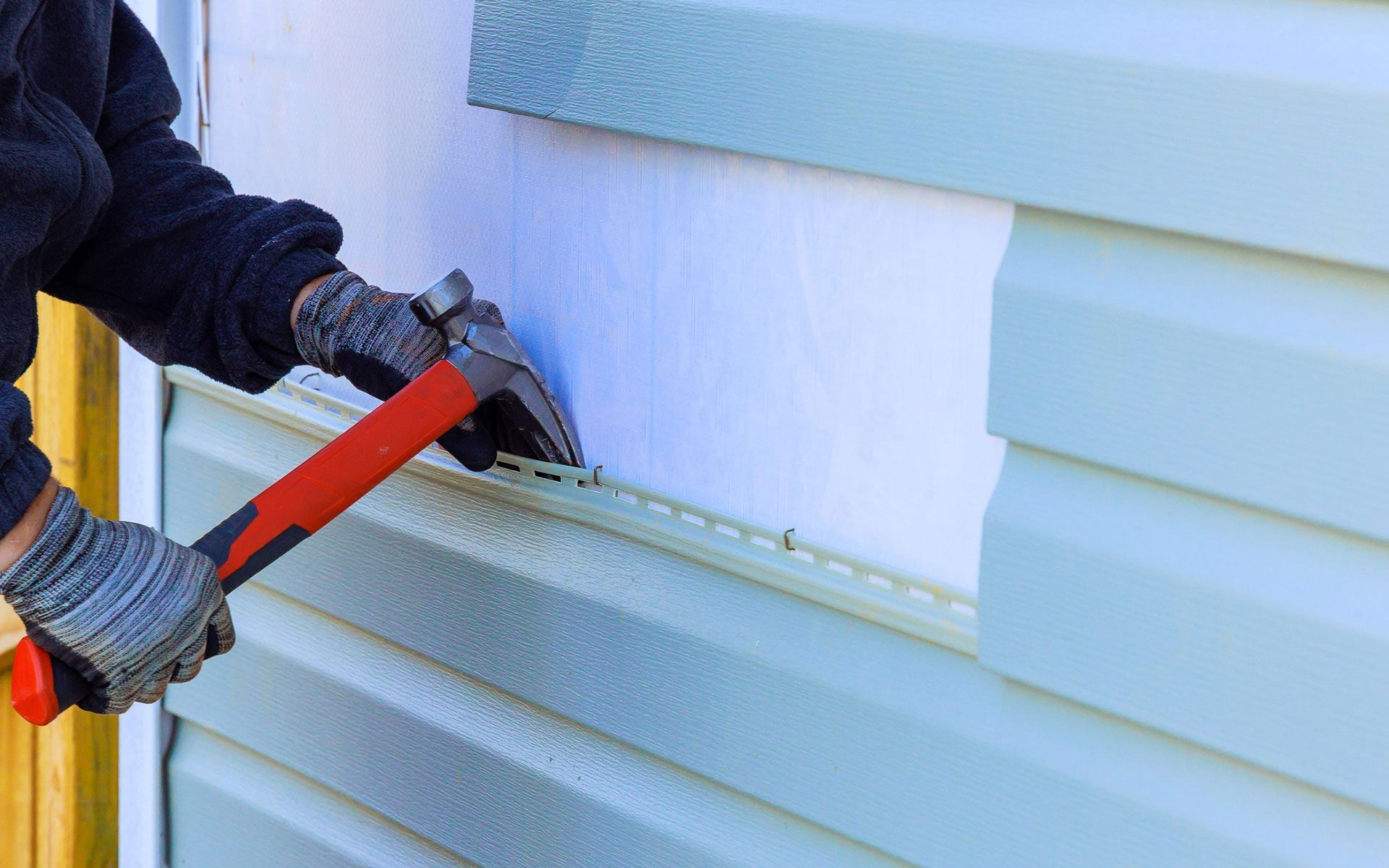 A man is installing siding on a house with a hammer.
