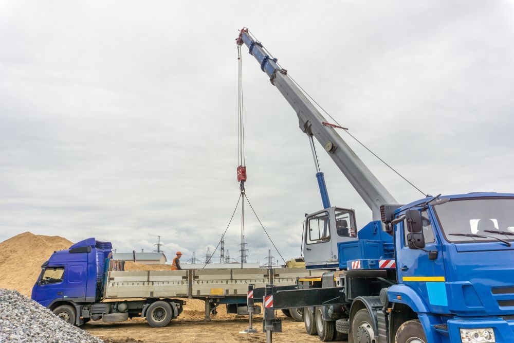Blue Cranes Lifting a Flatbed Truck in a Sandy Construction Yard — Barkly Hire in Kurumba, QLD