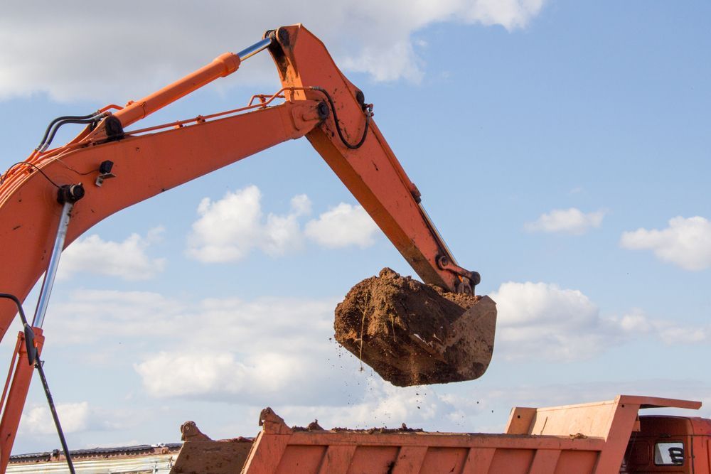 Orange Excavator Arm Lifting a Bucket of Dirt Over a Red Truck — Barkly Hire in Dugald River, QLD