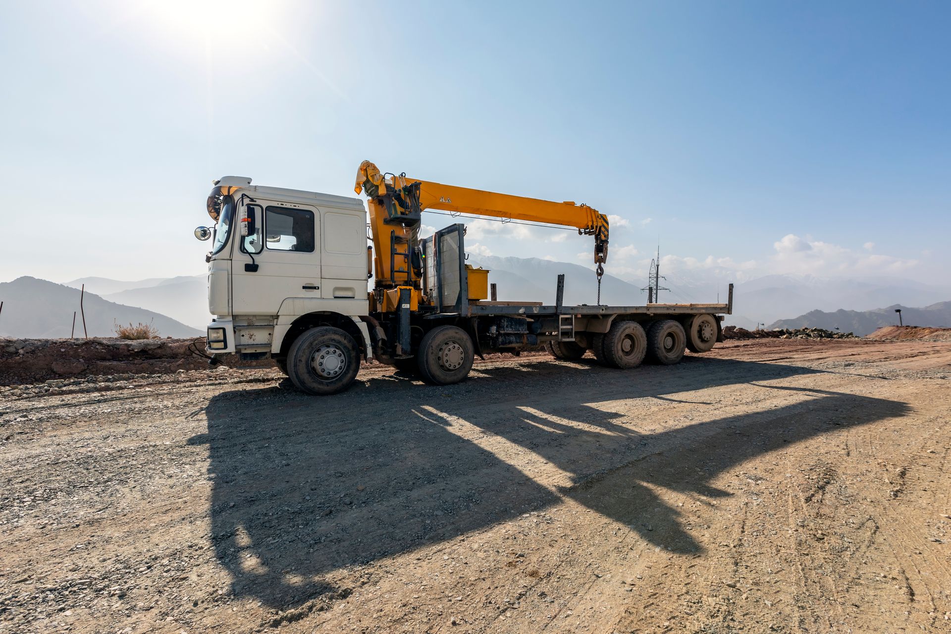 White Flatbed Truck With Yellow Crane Parked on a Gravel Construction Site — Barkly Hire in Cloncurry, QLD