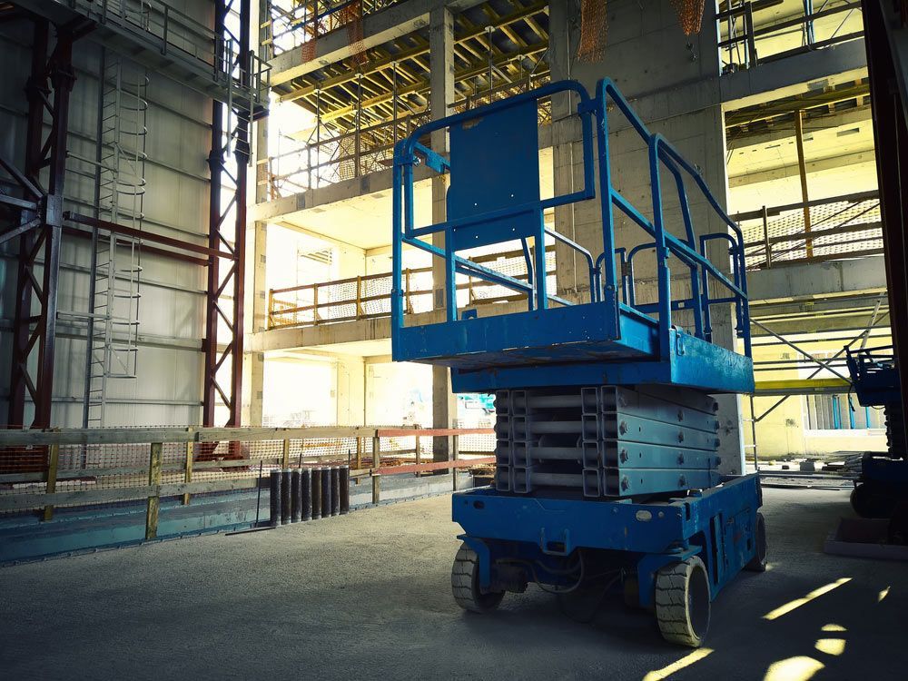 Blue Scissor Lift is Parked in Front of a Building Under Construction — Barkly Hire in Ryan, QLD