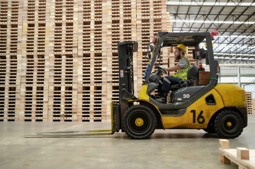 Man is Driving a Forklift in a Warehouse Filled With Wooden Pallets — Barkly Hire in Ryan, QLD