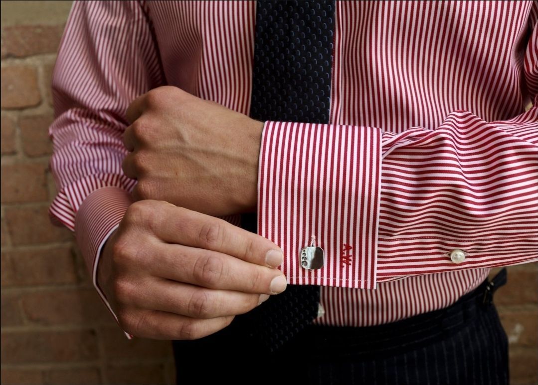 A man wearing a red and white striped shirt and tie is adjusting his cufflinks