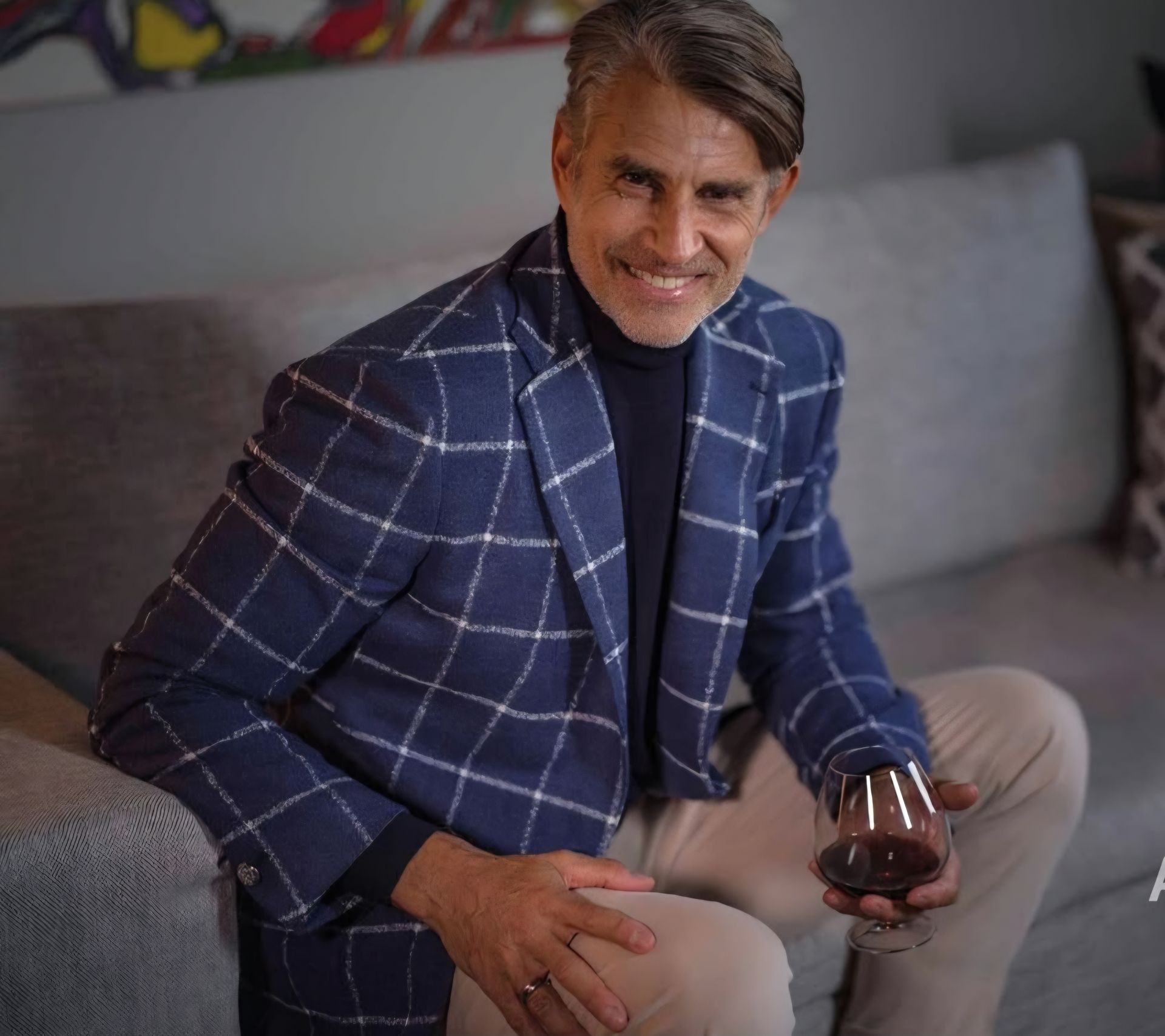 A man is sitting on a couch holding a glass of wine.