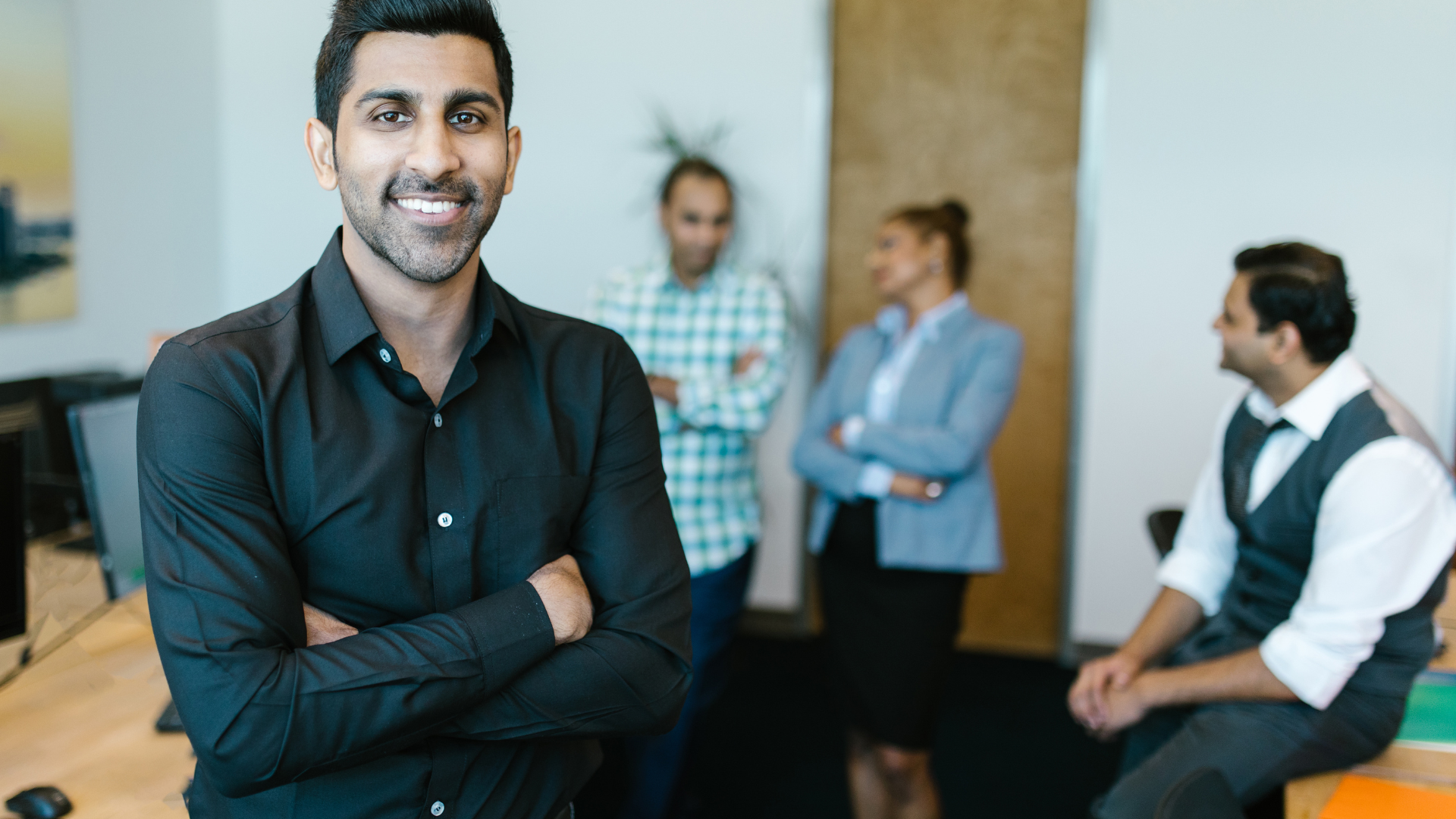 A man in a black shirt is standing with his arms crossed in front of a group of people.