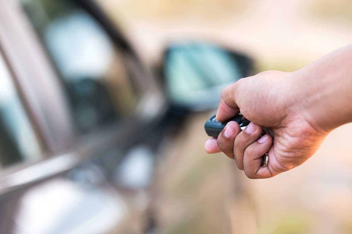 A person is holding a remote control in front of a car.