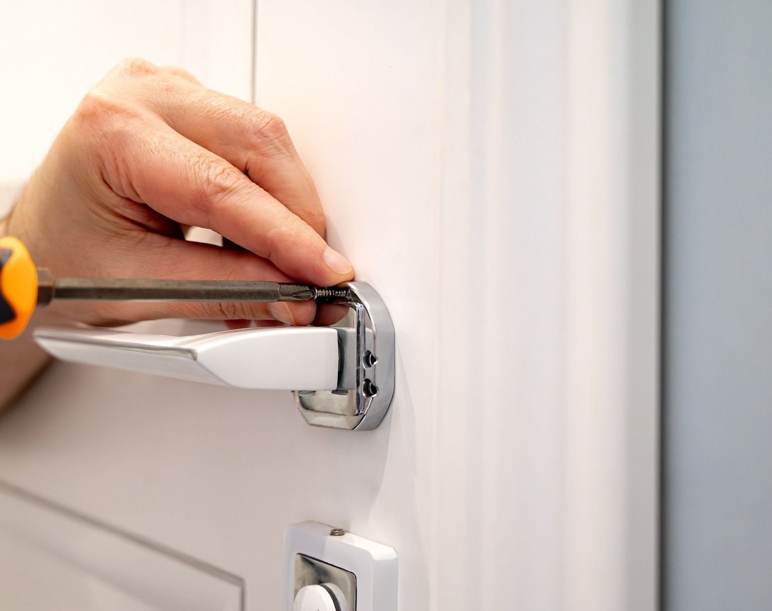 A person is fixing a door handle with a screwdriver.