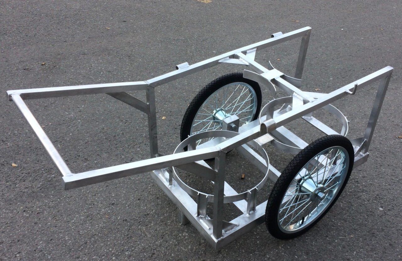 Un chariot en métal avec deux barils dessus est posé sur le sol.