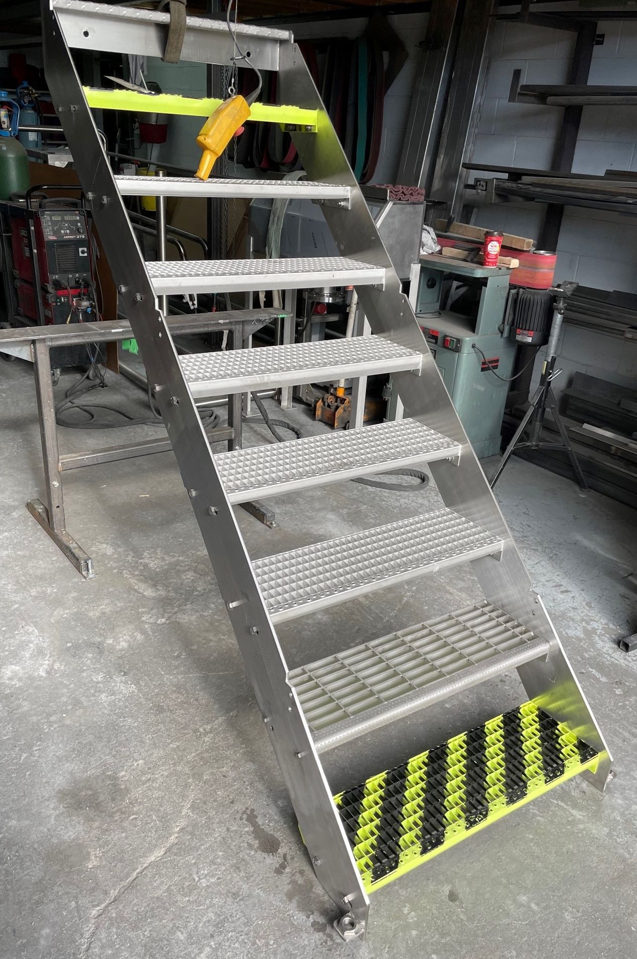 Un escalier en acier inoxydable avec des rayures jaunes et noires sur les marches se trouve dans un garage.