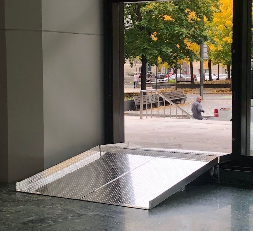 Une rampe en acier inoxydable menant à une rue avec des arbres en arrière-plan