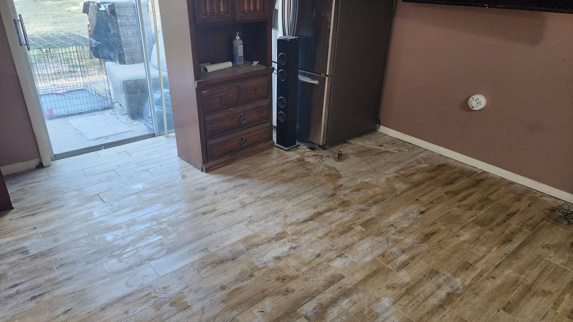 Room with light wood-look flooring and water damage, near a cabinet and doorway.