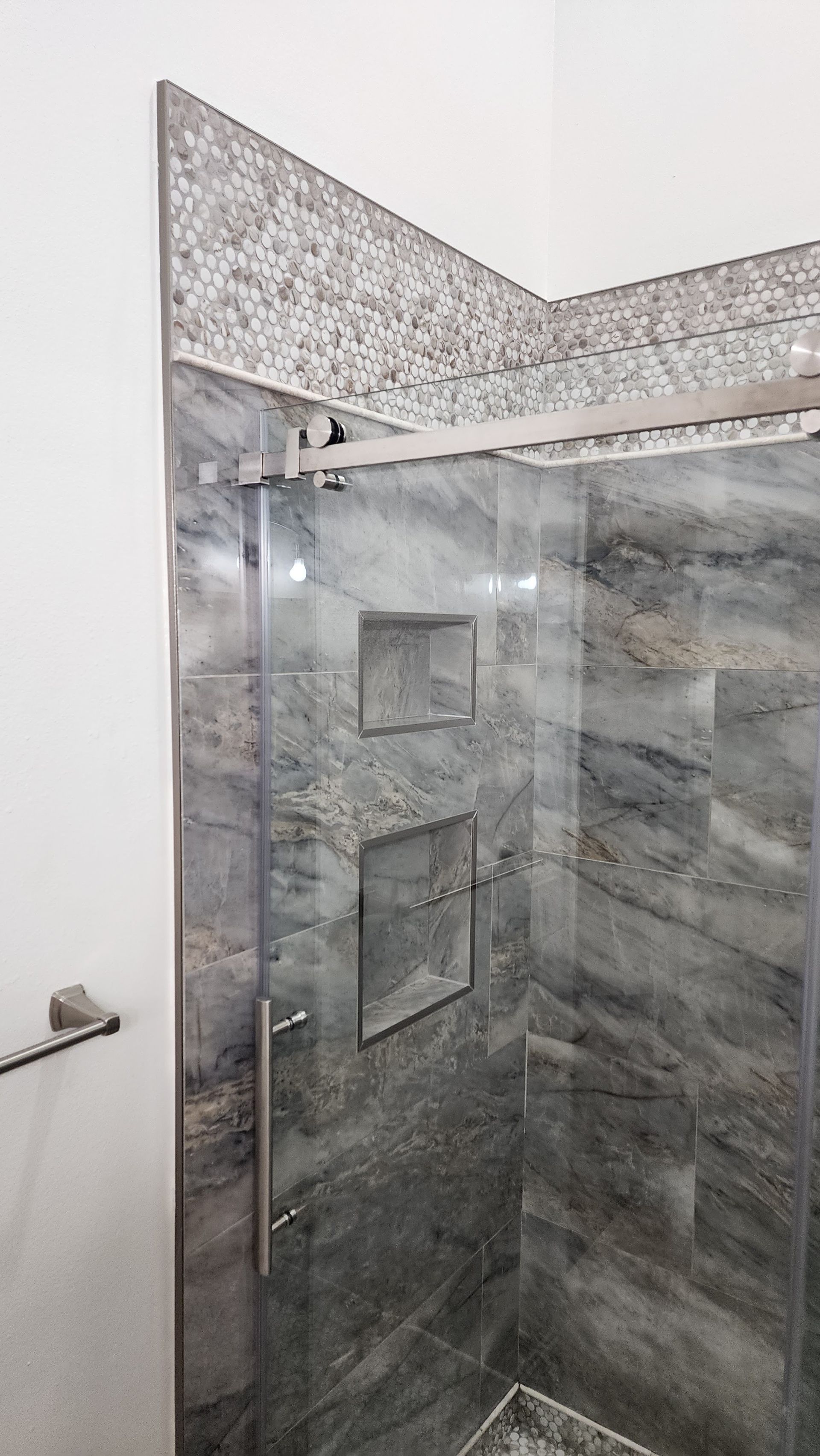 Corner shower with glass door and marble-look tile, featuring built-in niches.