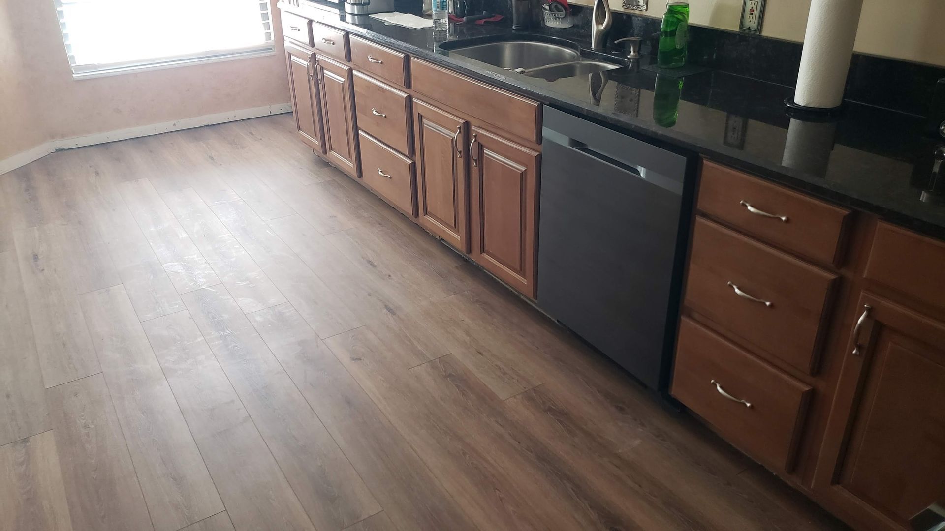 Kitchen with brown cabinets, black countertop, dishwasher, and wood-look flooring.