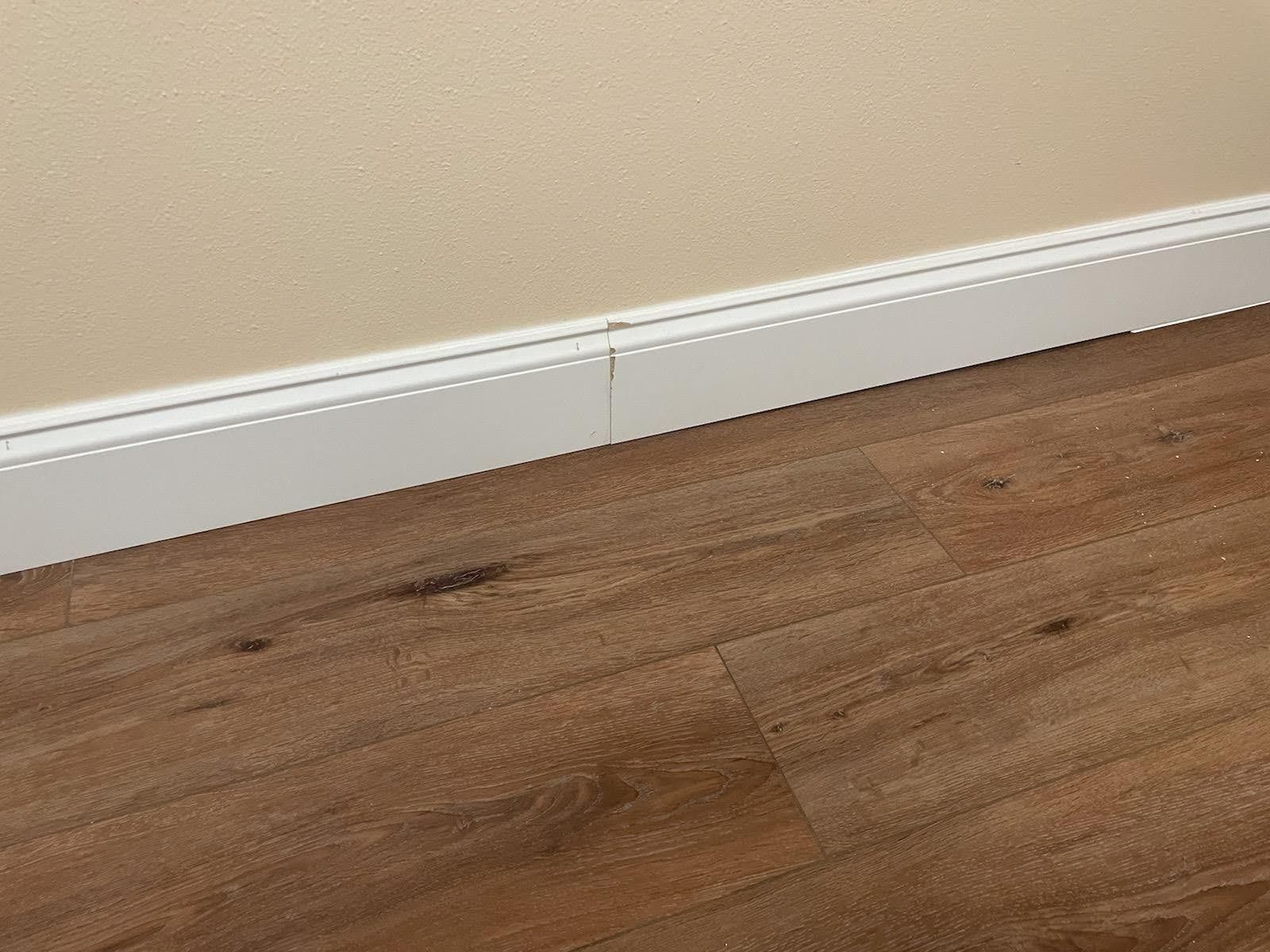 Brown wood flooring with white baseboards against a beige wall.